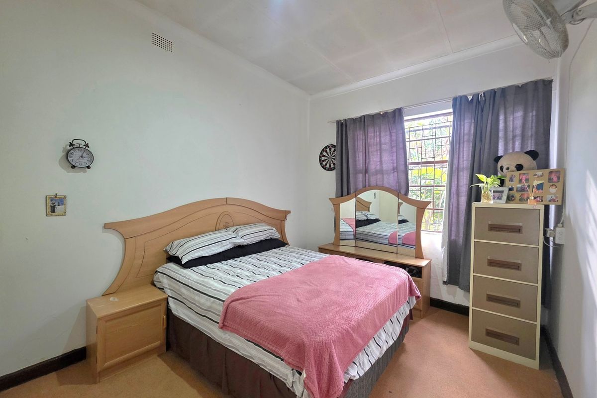 A functional bedroom featuring a window with security bars, a ceiling fan, and neutral wall finishes.
