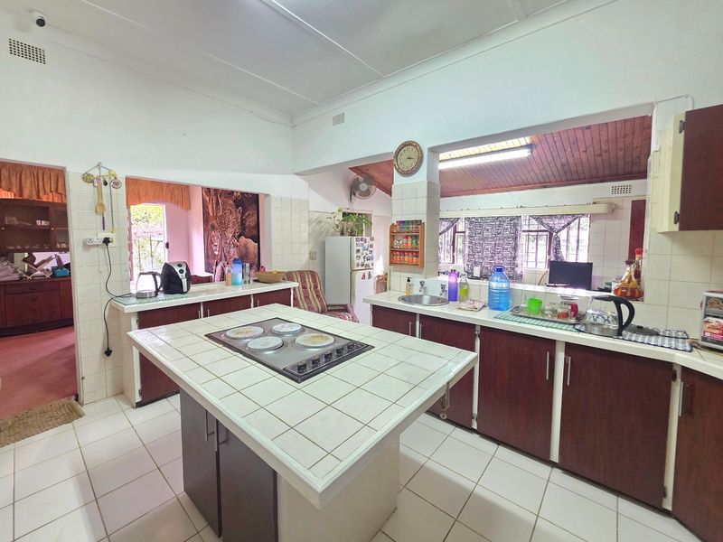 Spacious kitchen featuring a central island with built-in hob, tiled countertops, double sink, and ample cabinetry, offering a functional layout with potential for modernization.
