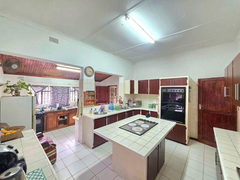 Spacious kitchen featuring a central tiled island with built-in hob, integrated oven, ample cabinetry, and tiled flooring, offering a functional layout for renovation.