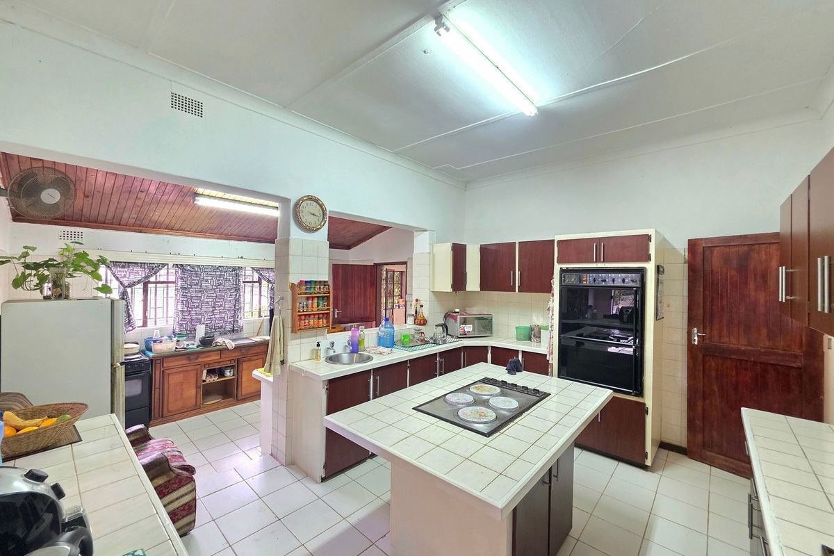 Spacious kitchen featuring a central tiled island with built-in hob, integrated oven, ample cabinetry, and tiled flooring, offering a functional layout for renovation.