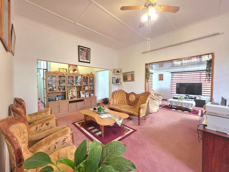 Spacious open-plan living area featuring a ceiling fan, coved cornicing, and large windows with fitted blinds, offering a versatile layout for family living.