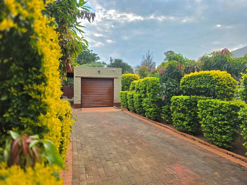 A well-maintained single garage with a brown sectional door, accessed via a paved brick driveway and framed by manicured garden hedges.
