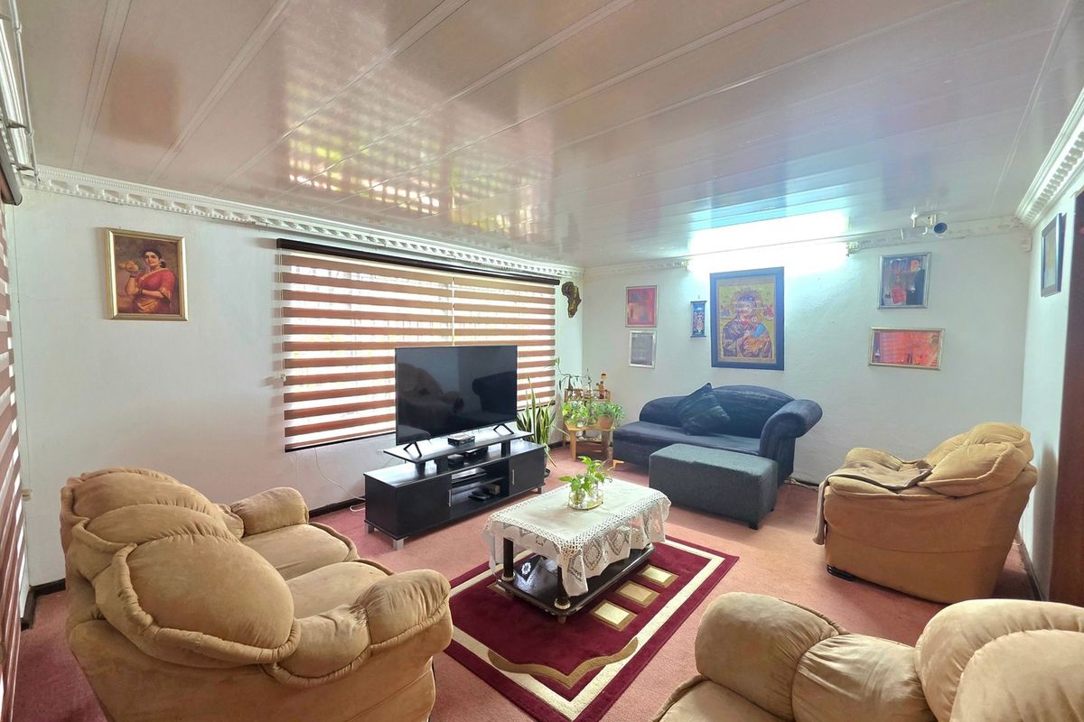 A comfortable living room featuring glossy ceiling panels, decorative cornice detailing, and large windows fitted with modern venetian blinds.