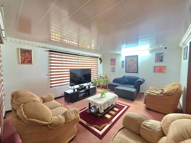 A comfortable living room featuring glossy ceiling panels, decorative cornice detailing, and large windows fitted with modern venetian blinds.