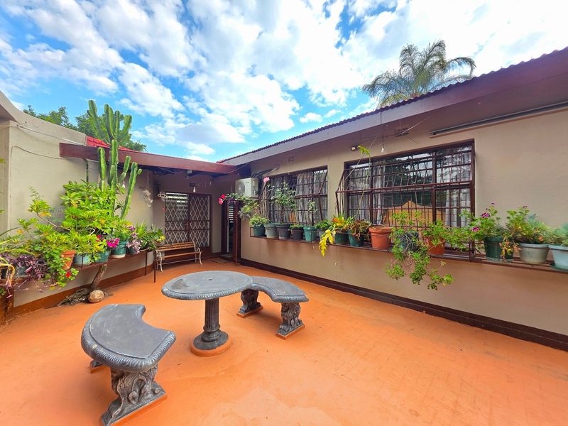 A covered outdoor patio area featuring concrete flooring, security bars on windows, and an exterior air conditioning unit.