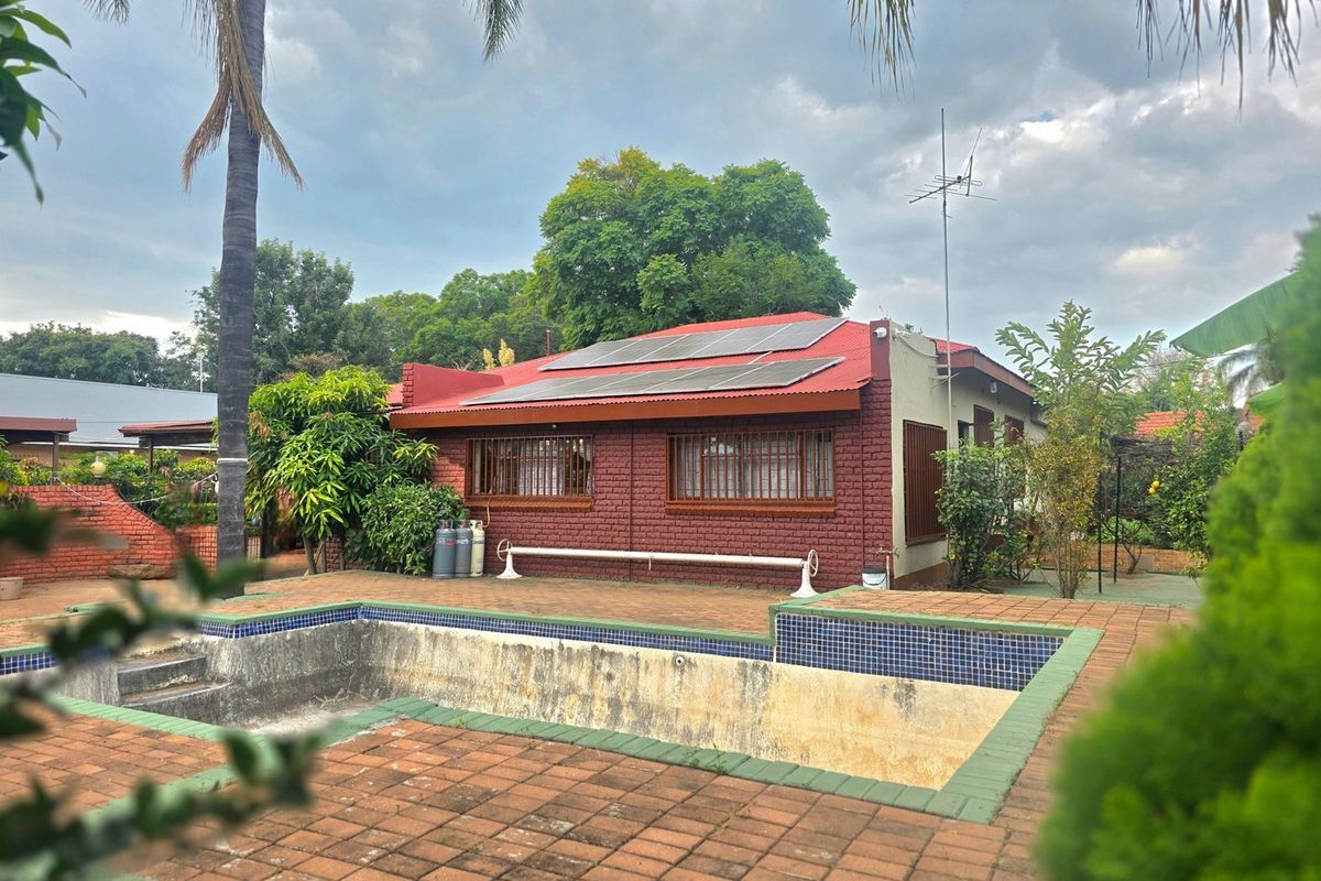Rear view of the property featuring a brick facade, solar panels, and an in-ground swimming pool with paved surround.