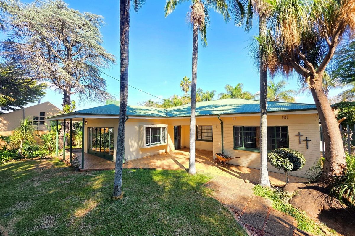 Rear view of the house featuring a covered patio, paved walkway, and established garden with mature palm trees.