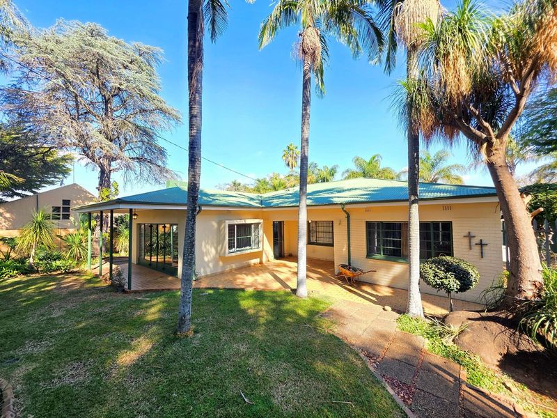 Rear view of the house featuring a covered patio, paved walkway, and established garden with mature palm trees.