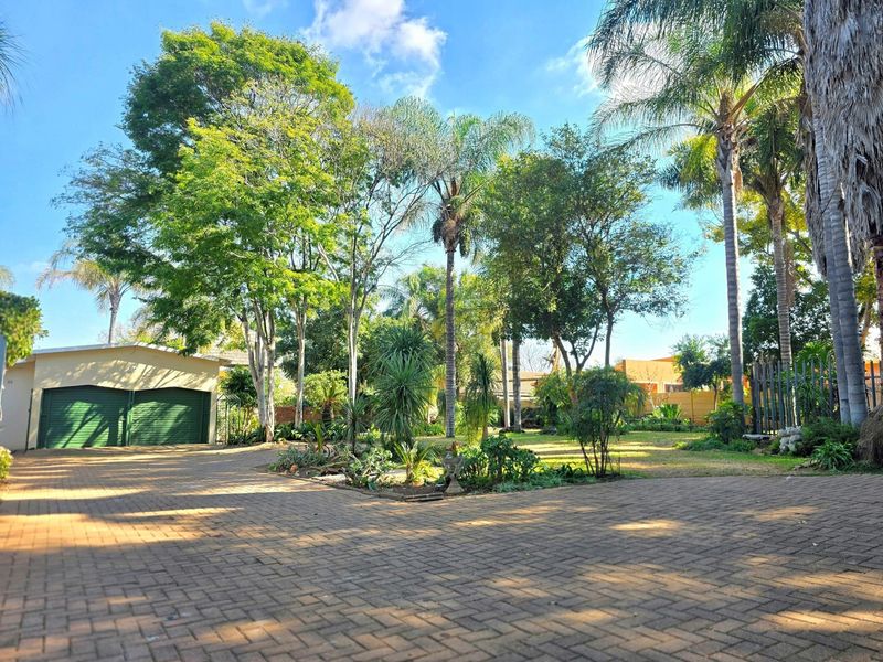 Spacious front exterior featuring a large paved driveway, double garage, and a well-established garden with mature trees.