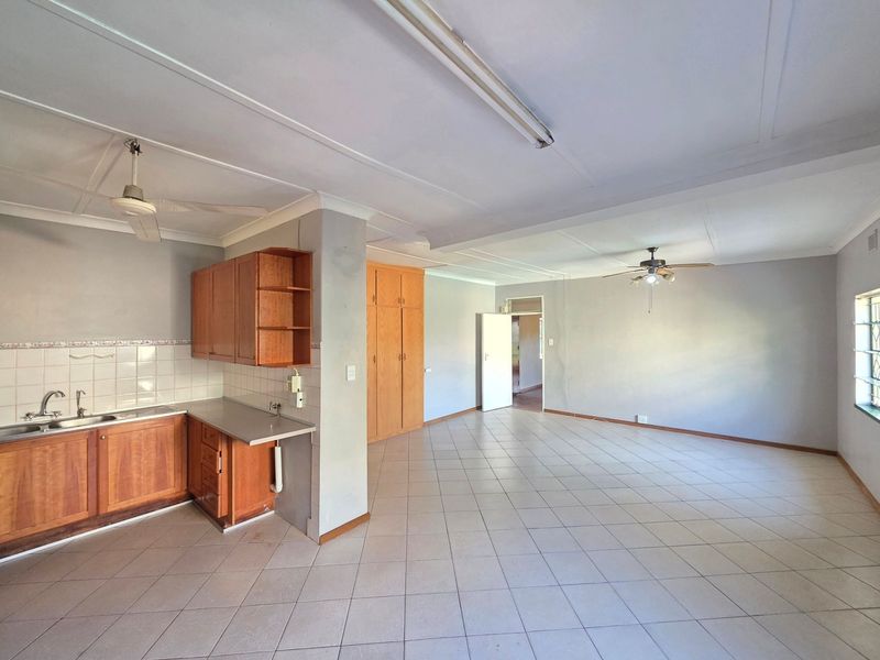Spacious open-plan living and kitchen area featuring tiled flooring, built-in wooden cabinetry, and ceiling fans, offering a blank canvas for renovation.