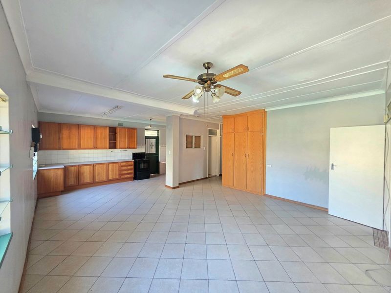 Spacious open-plan living and kitchen area featuring tiled flooring, wooden cabinetry, built-in cupboards, and a ceiling fan.