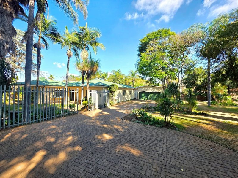 Front view of the property featuring a paved driveway, established garden, metal security fencing, and a double garage.