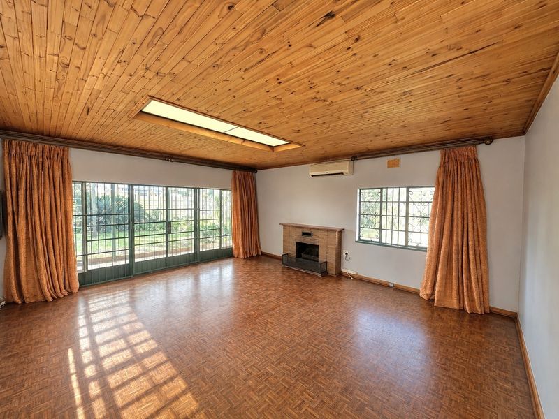 Spacious living room featuring parquet flooring, a timber ceiling with a skylight, a brick fireplace, and large sliding doors leading to the garden.