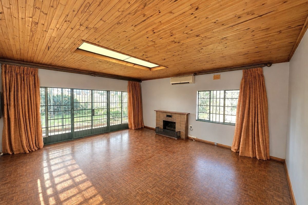 Spacious living room featuring parquet flooring, a timber ceiling with a skylight, a brick fireplace, and large sliding doors leading to the garden.