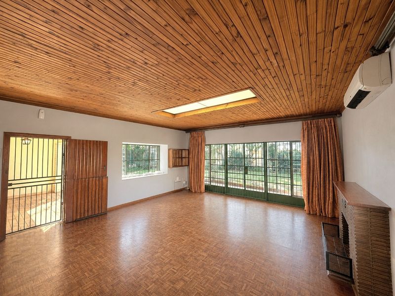 Spacious living room featuring parquet flooring, a timber-clad ceiling with a skylight, a brick fireplace, and direct access to the garden through sliding doors.