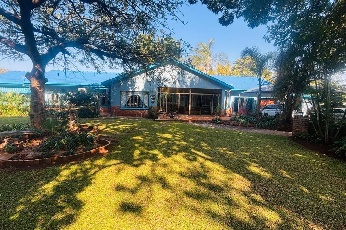 Rear view of the house featuring a blue metal roof, brick exterior, and large sliding glass doors opening onto a spacious, well-maintained garden.