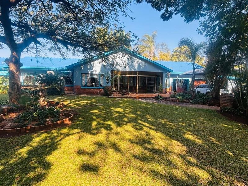 Rear view of the house featuring a blue metal roof, brick exterior, and large sliding glass doors opening onto a spacious, well-maintained garden.