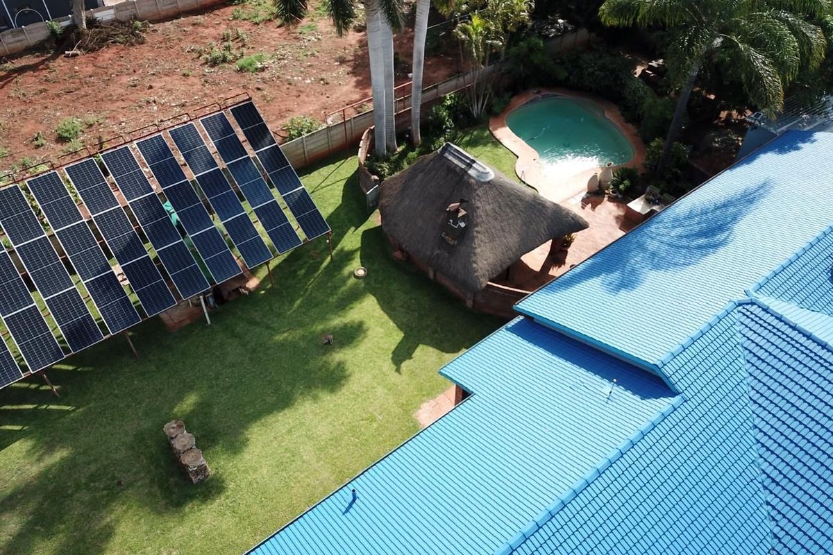 Aerial view of the property featuring a large solar panel array, a swimming pool, a thatched lapa, and a well-maintained garden area.