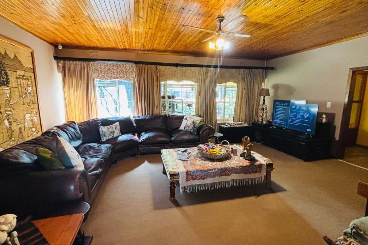 Spacious living room featuring a warm timber tongue and groove ceiling, ceiling fan, and neutral carpeting, offering a comfortable and inviting atmosphere.