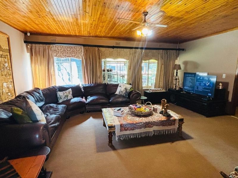 Spacious living room featuring a warm timber tongue and groove ceiling, ceiling fan, and neutral carpeting, offering a comfortable and inviting atmosphere.