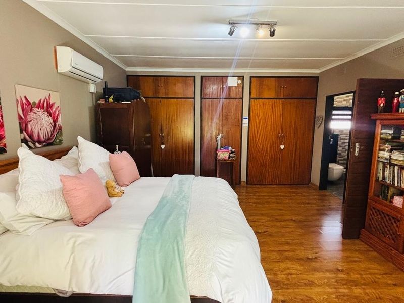 Spacious bedroom featuring built-in wooden cupboards, laminate flooring, and an integrated air conditioning unit, with direct access to an en-suite bathroom.