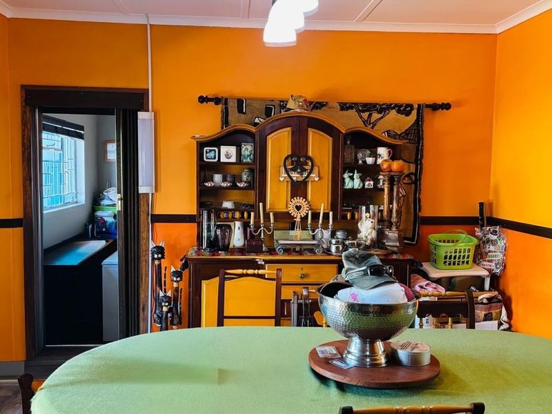 A dining room featuring bold orange walls with a dark dado rail, leading into an adjacent utility or scullery area.