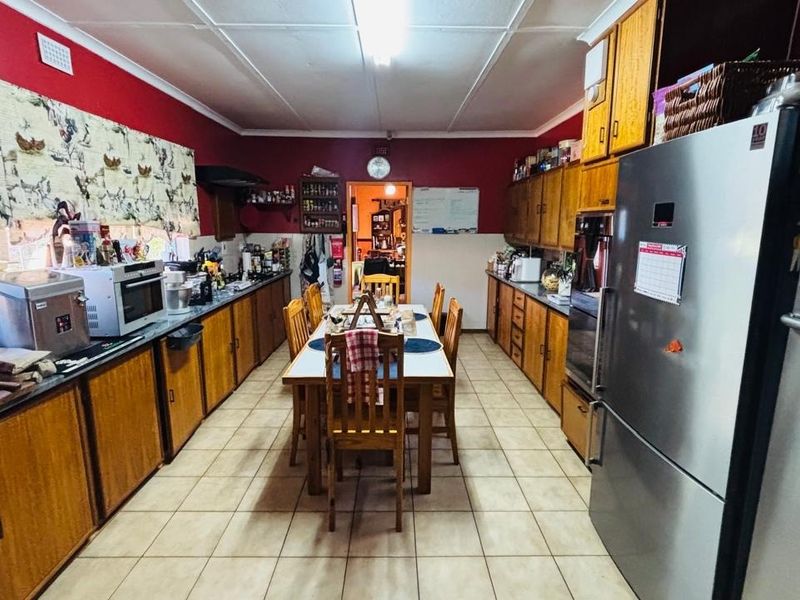Spacious kitchen featuring extensive built-in wooden cabinetry, tiled flooring, and integrated appliances, offering a functional layout with potential for modern updates.