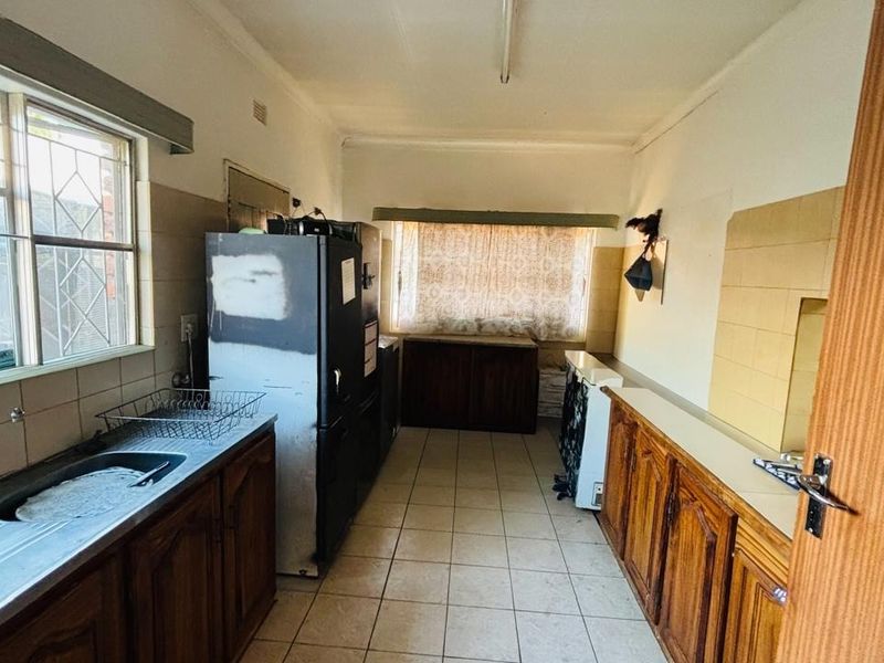 A dated kitchen featuring original wooden cabinetry, tiled splashbacks, and tiled flooring, offering significant potential for a modern renovation and layout update.