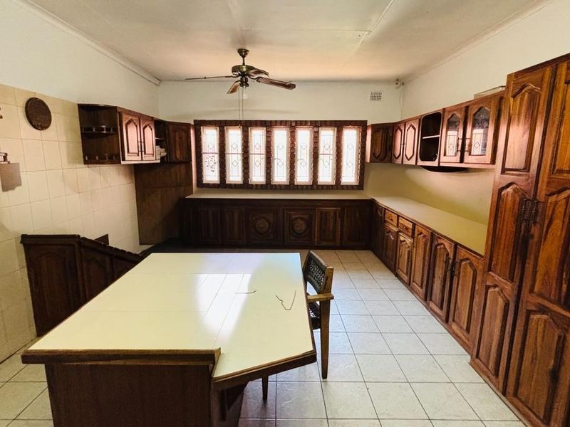 A spacious kitchen featuring extensive wooden cabinetry, tiled flooring, a central island, and a ceiling fan, offering a traditional layout with ample storage.