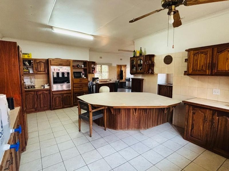 Spacious kitchen featuring extensive built-in wooden cabinetry, a central island, tiled flooring, and a built-in oven, offering a functional layout with dated finishes.