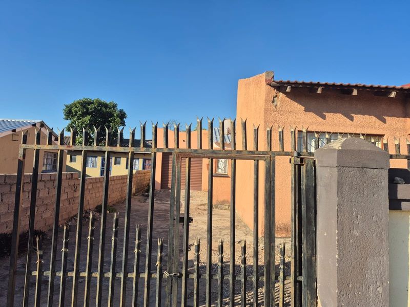 Front view of the property featuring a metal security gate, boundary wall, and stucco exterior finish with visible signs of weathering.