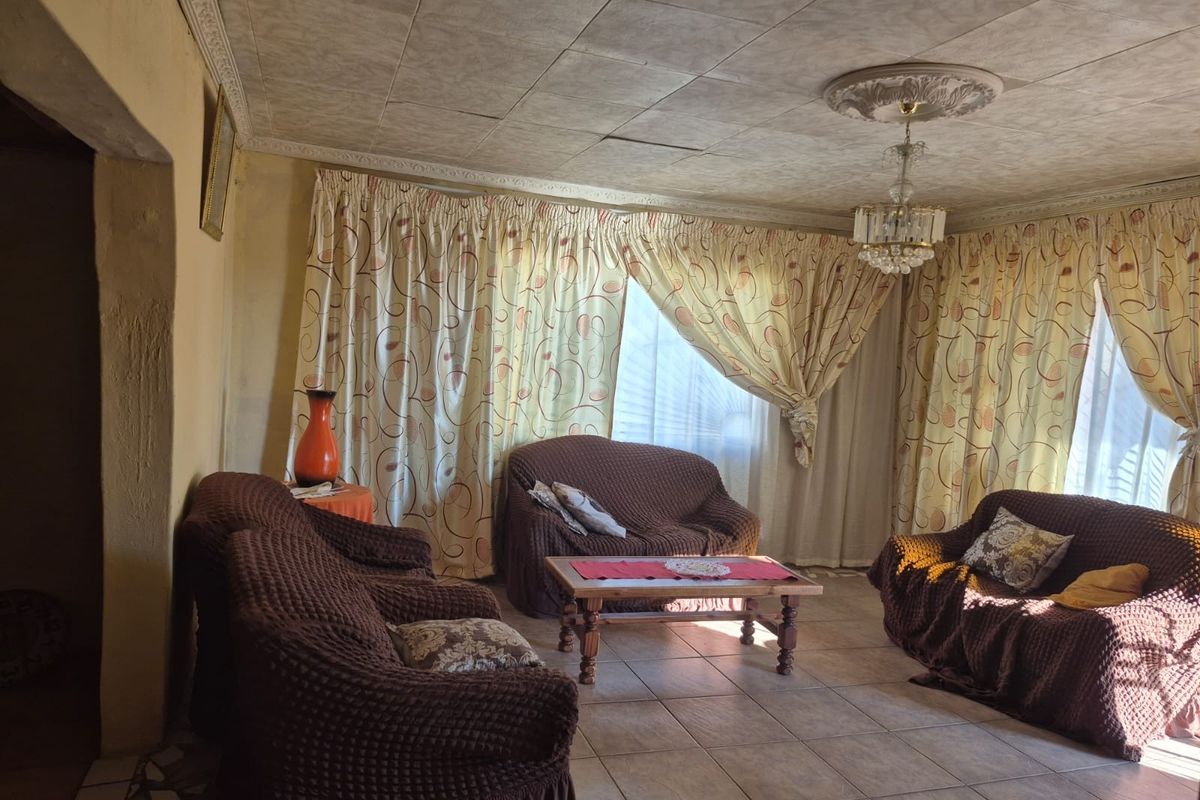 A living room featuring tiled flooring, decorative ceiling tiles with a central rose, and coving, requiring cosmetic updates to improve the overall aesthetic.