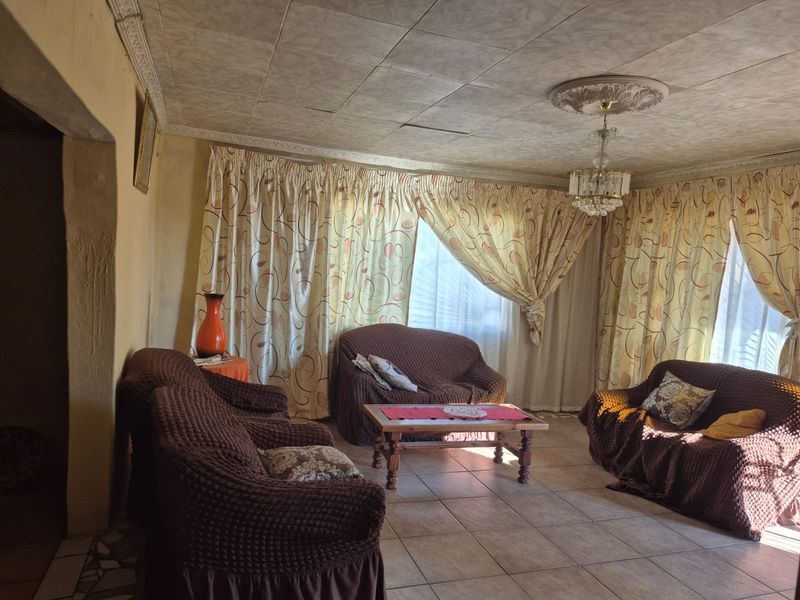 A living room featuring tiled flooring, decorative ceiling tiles with a central rose, and coving, requiring cosmetic updates to improve the overall aesthetic.