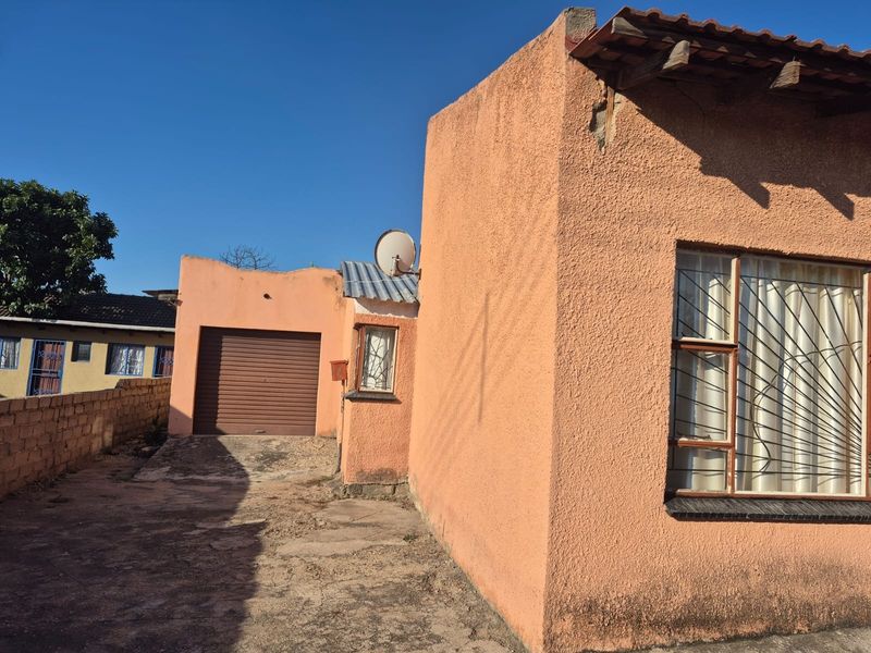 Rear exterior view of the property featuring a garage, concrete driveway, and textured peach-colored walls with security bars on the windows.
