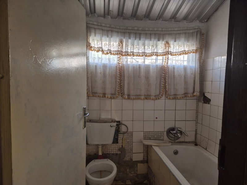 A dated bathroom featuring a bathtub and toilet with visible wall tile damage and exposed structural elements, requiring renovation.