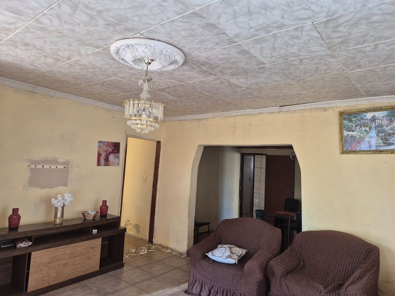 Living room featuring decorative ceiling rose, cornice detailing, and tiled flooring, currently requiring cosmetic updates and wall repairs.