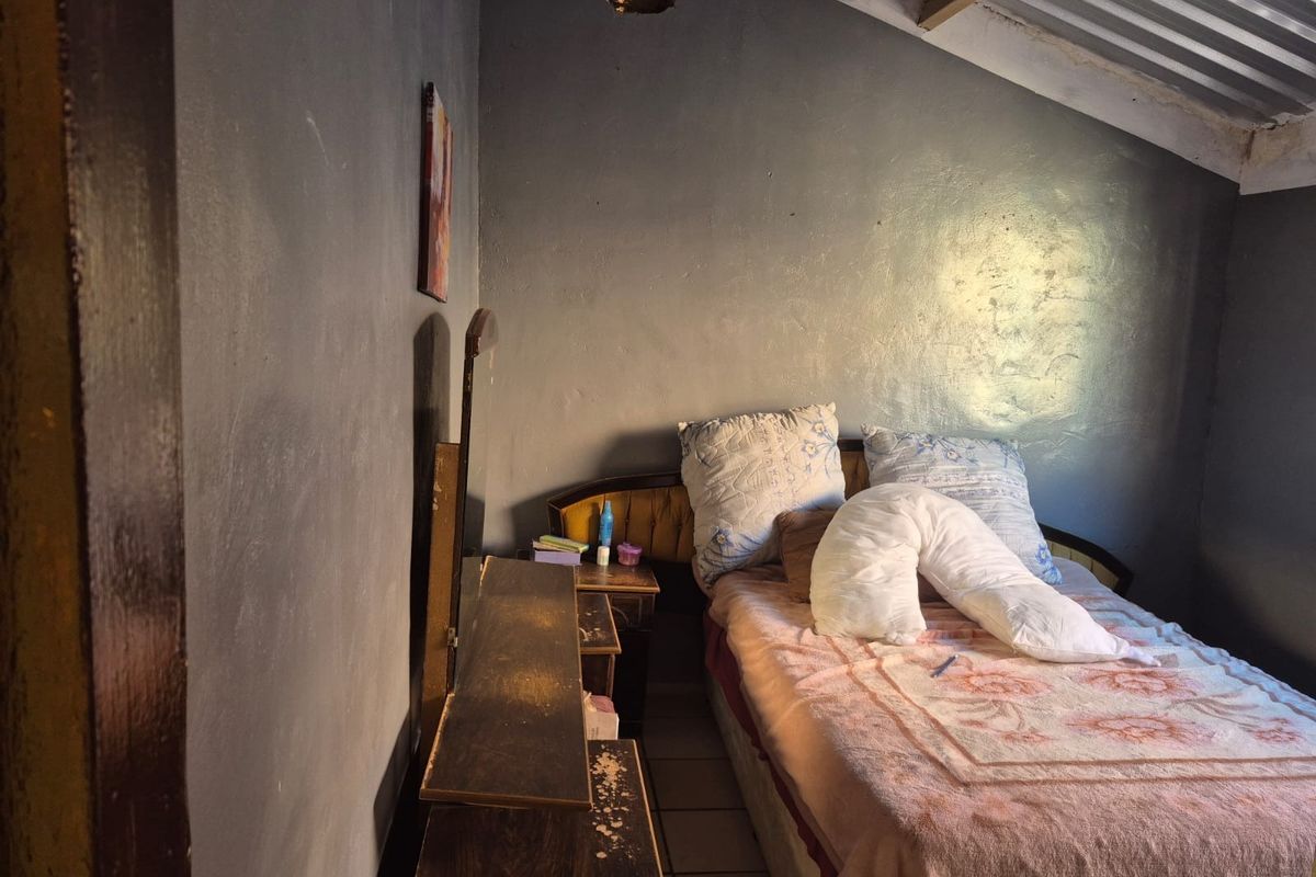A bedroom featuring tiled flooring and an exposed corrugated metal roof, requiring significant cosmetic updates and ceiling repairs to improve the living space.