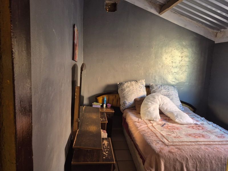 A bedroom featuring tiled flooring and an exposed corrugated metal roof, requiring significant cosmetic updates and ceiling repairs to improve the living space.