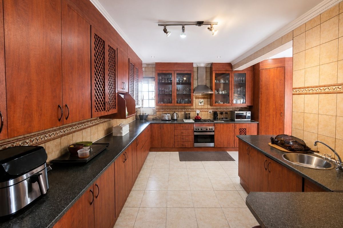 Spacious kitchen featuring extensive wooden cabinetry, granite countertops, built-in oven with extractor fan, and tiled flooring with a functional layout.