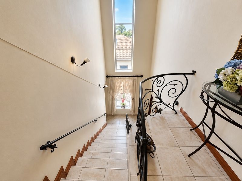 A bright staircase featuring tiled steps, a decorative wrought iron balustrade, and a tall vertical window that allows for ample natural light.