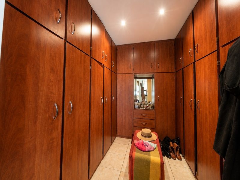 A walk-in dressing room featuring extensive floor-to-ceiling wooden built-in cabinetry, tiled flooring, and integrated recessed lighting.