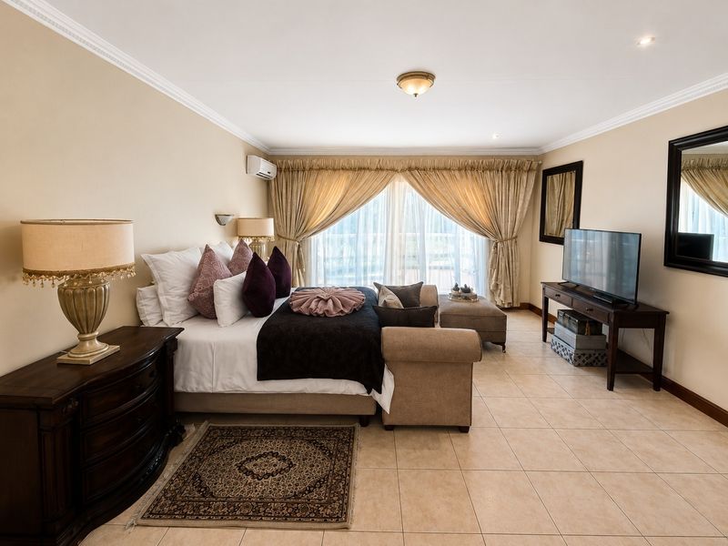 Spacious bedroom featuring neutral tiled flooring, crown molding, and a wall-mounted air conditioning unit, offering a comfortable and well-maintained living space.