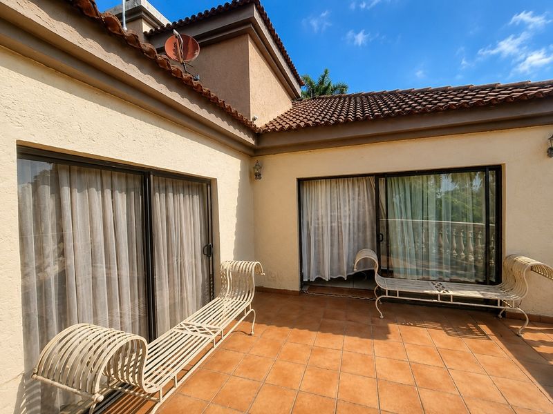 A spacious outdoor patio featuring terracotta tiling, sliding glass door access to the interior, and traditional terracotta roof detailing.