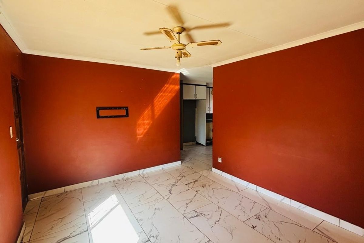 An empty living room featuring marble-look floor tiles, a ceiling fan, and a recessed wall niche, finished with bold red wall paint.