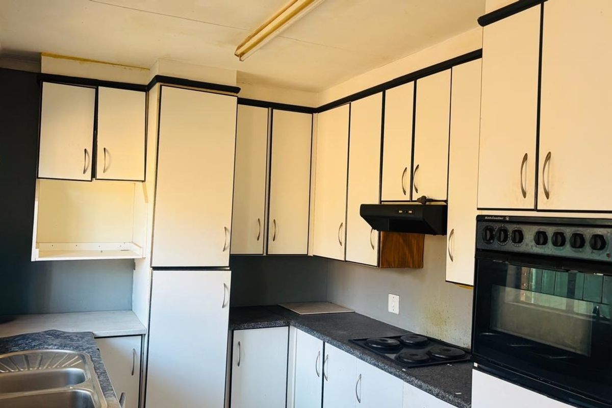A dated kitchen featuring white cabinetry with black trim, laminate countertops, a built-in oven, and an electric hob, offering potential for modern renovation.