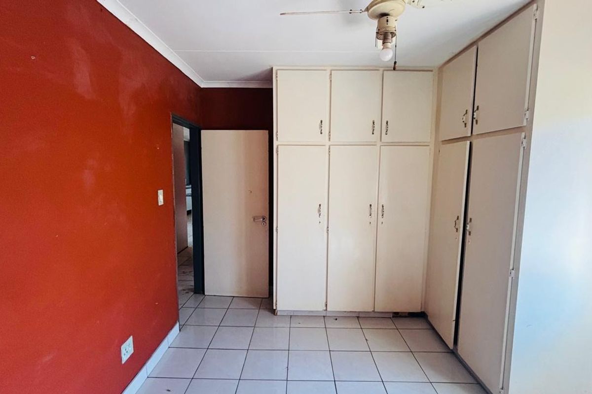 A vacant bedroom featuring tiled flooring, built-in cupboards, and a ceiling fan, ready for a fresh coat of paint and modern updates.