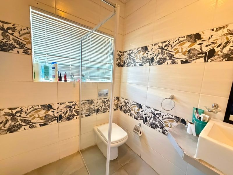 A compact bathroom featuring a wall-mounted toilet, glass shower screen, and decorative tiled walls with a modern basin.