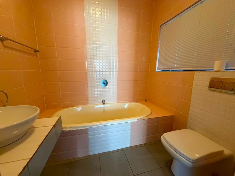 A dated bathroom featuring a built-in bathtub, wall-mounted toilet, and vessel sink, finished with peach and white wall tiles.
