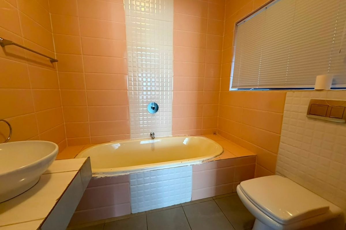 A dated bathroom featuring a built-in bathtub, wall-mounted toilet, and vessel sink, finished with peach and white wall tiles.