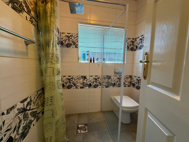 Compact bathroom featuring a walk-in shower with a rain shower head, glass screen, wall-mounted toilet, and decorative tiled wall accents.